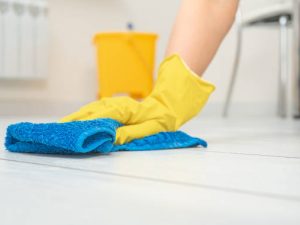 Cleaning service. crop image of woman thoroughly and gently washing and cleaning white laminate floor. female hands in yellow gloves wipe wooden floor with blue microfiber cloth. copy space