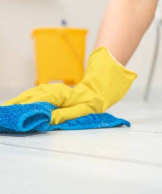 Cleaning service. crop image of woman thoroughly and gently washing and cleaning white laminate floor. female hands in yellow gloves wipe wooden floor with blue microfiber cloth. copy space